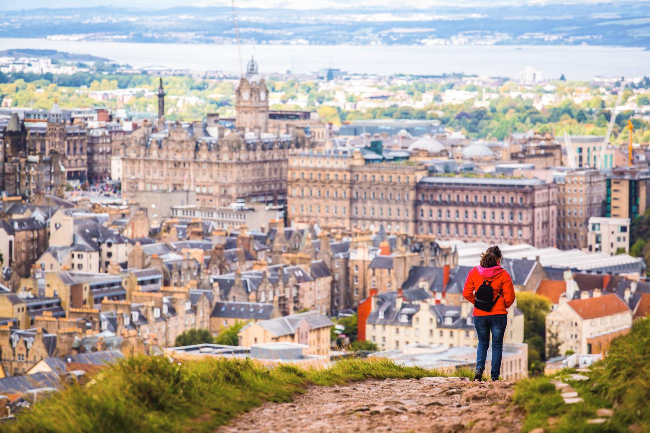 The city of Edinburgh skyline with a women wearing a red jacket in the foreground.