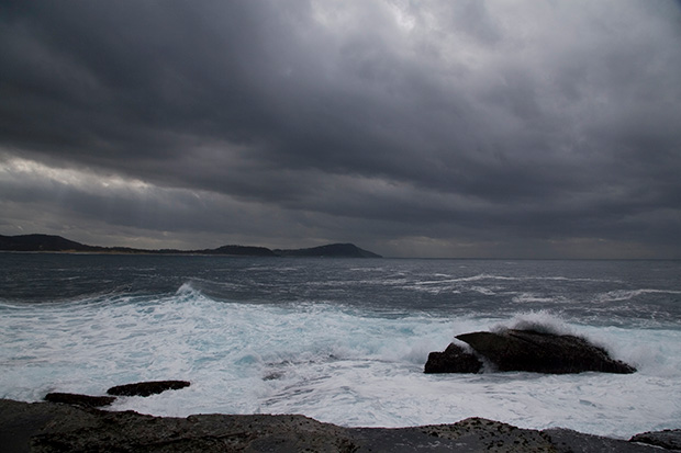 Sea view of waves crashing on rocks and a cloudy sky.