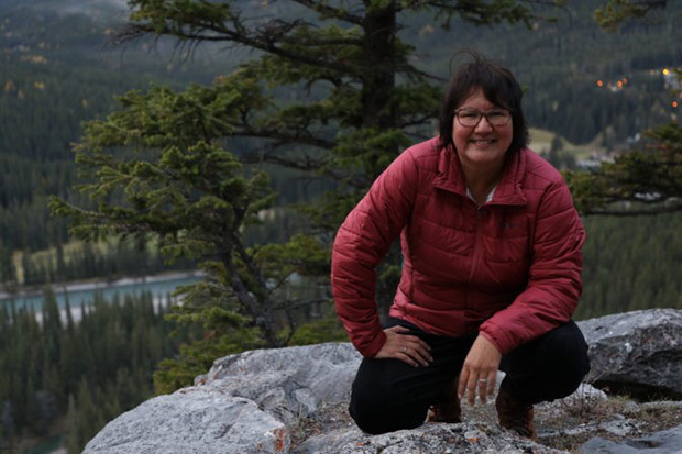 A women in a red jacket sits atop a rock.