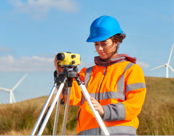 An engineer on site at a wind farm using equipment in a high vis jacket.