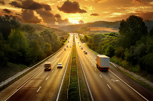 Vehicles drive down a motorway into the sunset.