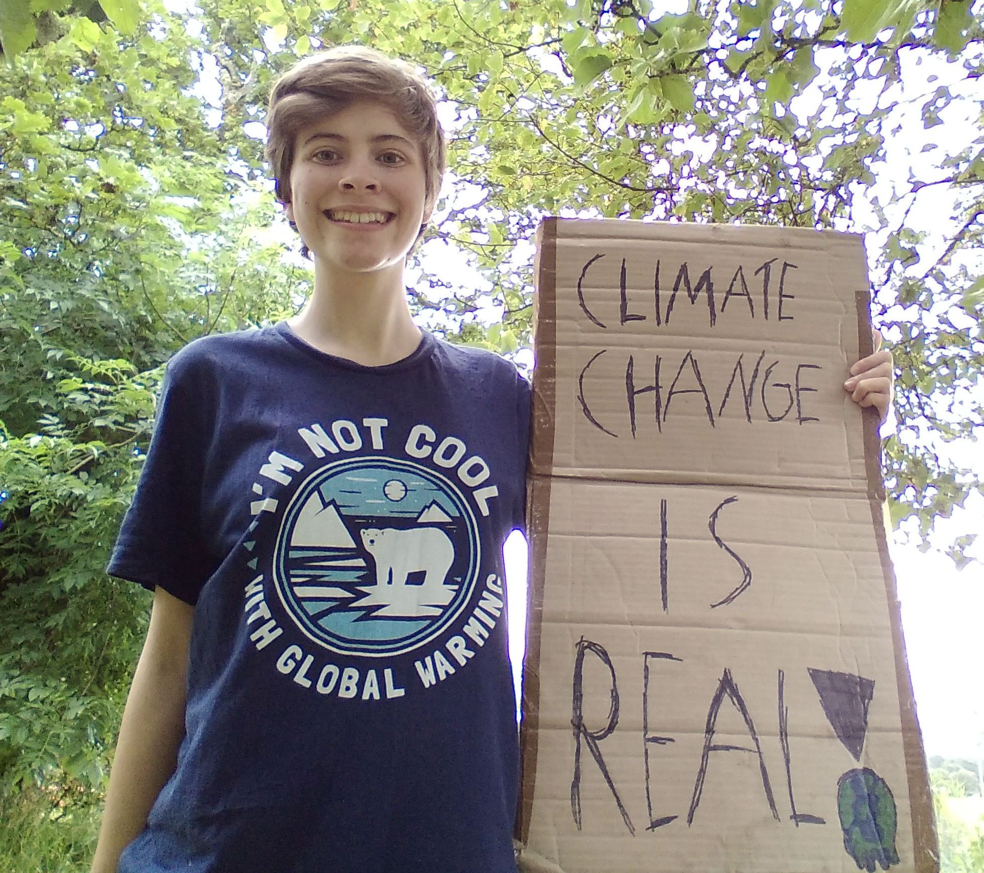 Photo of a young girl holding a cardboard sign that reads "climate change is real!"