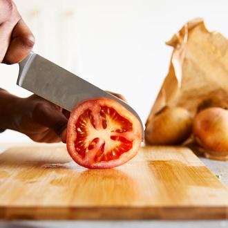 A person chopping a tomato on a wooden chopping board.