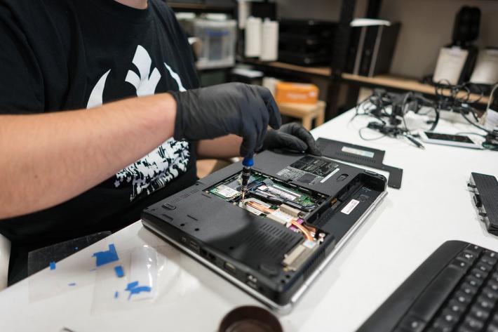 A person wearing black gloves fixing a laptop.