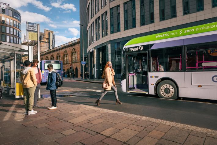 People wait to board a bus on a busy Glasgow street.