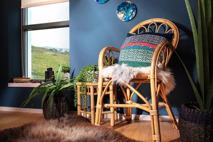 A wicker chair with a sheepskin rug on it, in a blue room with a brown sheepskin rug on the floor