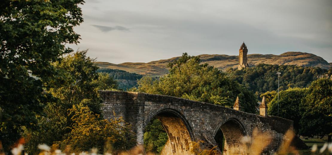 A bridge and trees nearby the Stirling hills and Wallace monument