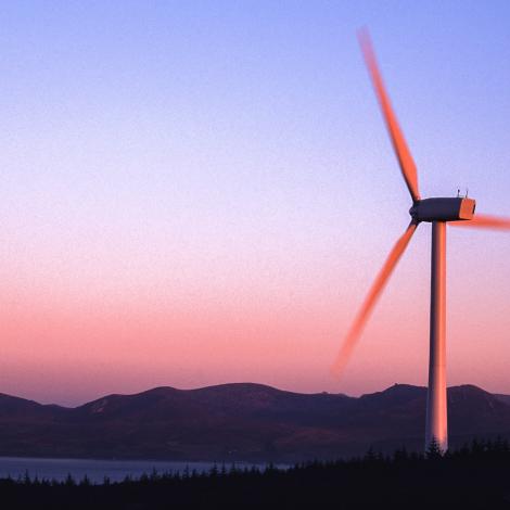 A wind turbine set against a mountain backdrop, at sunset