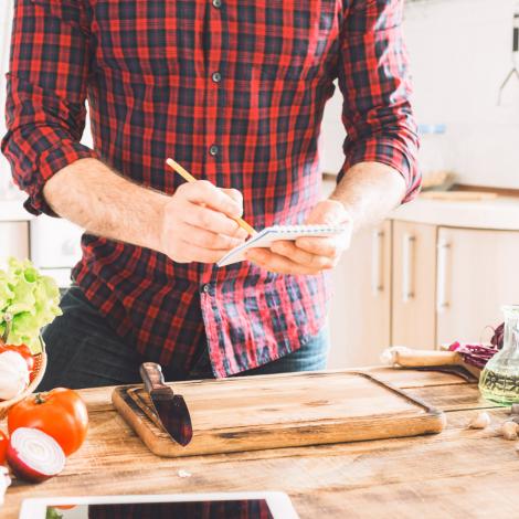 A man in a checked shirt writing on a shopping list