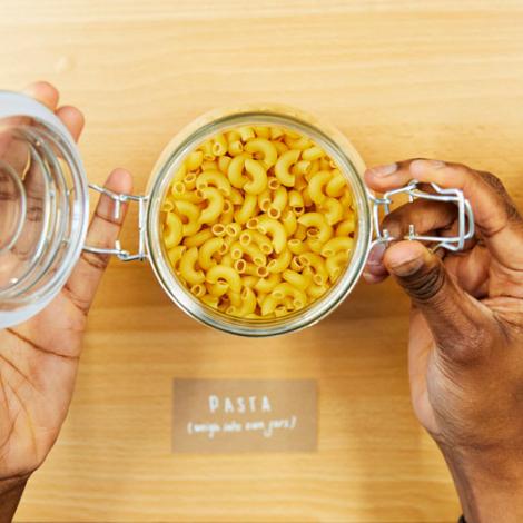 A pair of hands opening a jar of dried macaroni pasta