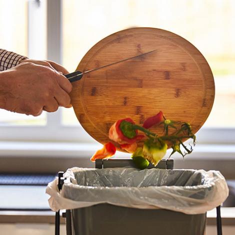 A person scraping food off a chopping board into a food bin.